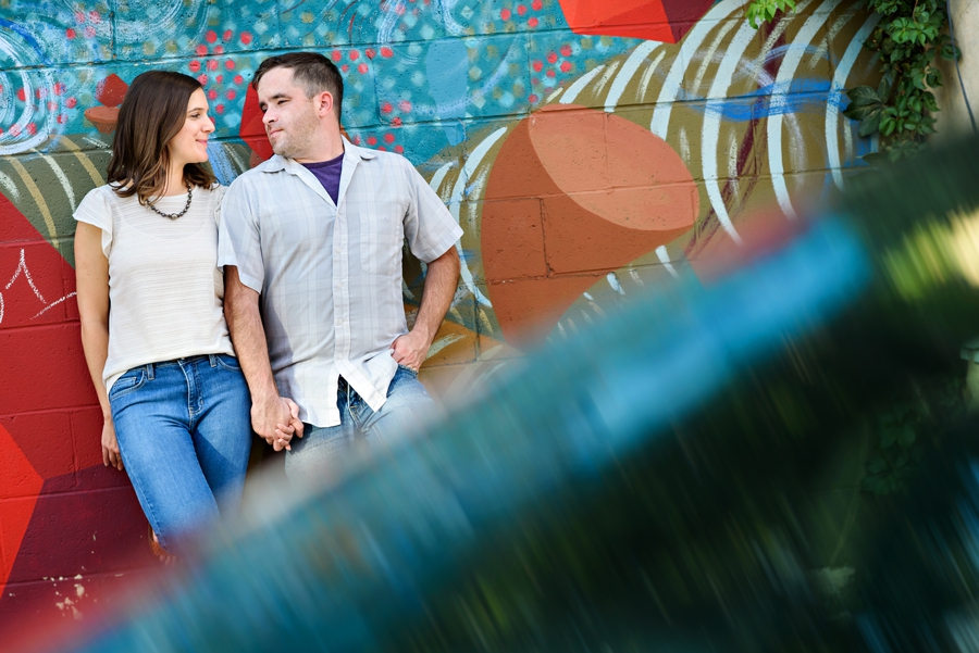 A man and woman lean against a graffiti wall and look into each other's eyes.
